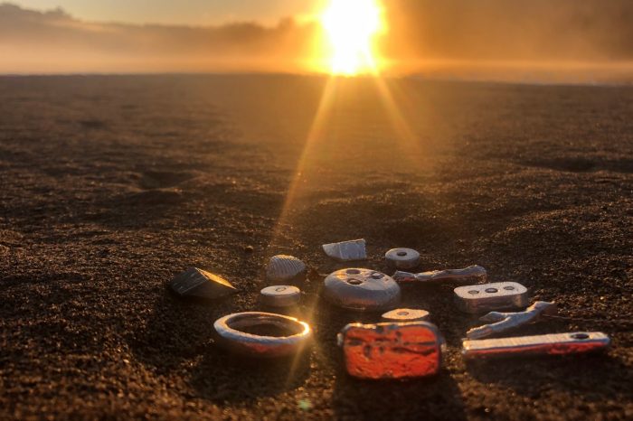 A collection of assorted metals on sand with the sun setting in the background.