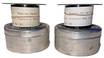 A photograph of two microfilm rolls which contain books. One is Hopalong Cassidy by Clarence C Mulford, and the other is Windows for the Crown Prince by Elizabeth Gray Vining. The microfilm rolls are labelled, and sit atop circular storage tins.
