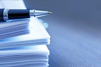 A ballpoint pen rests on top of a stack of documents ready for signing.  The image is photographed using a very shallow depth of field with the focus being on the tip of the pen.