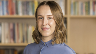 Researcher Elena Cama stands in front of a bookcase, a quietly confident expression on her face.