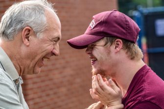 Elderly man embracing student with disability