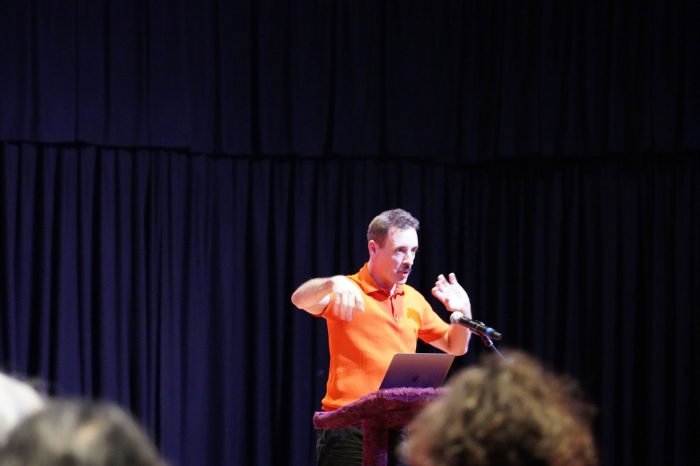 presenter wearing orange polo speaking at lectern