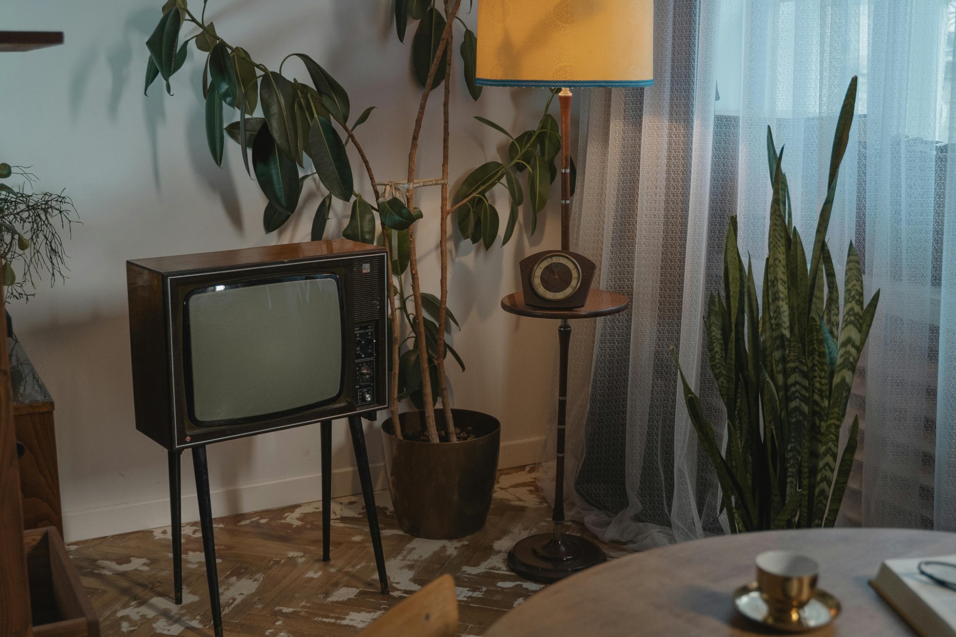 A brown vintage CRT on legs stands to the left of a lighted yellow lamp in a 70s style room