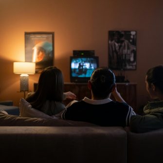 Three people sit on a couch in a dimly lit loungeroom watching a movie on a small TV screen
