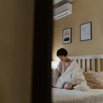 A woman sits in bed with a white blanket around her shoulders