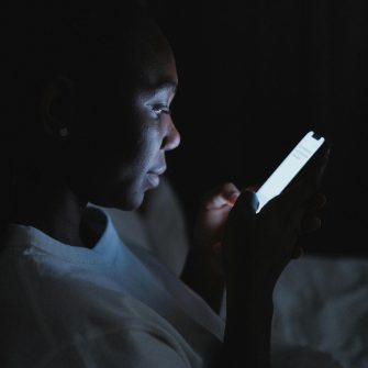 A woman sits in a dark room using a smartphone