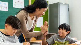 Young Asian teacher giving boy high five in school, success, achievement, happiness. Asia school boy with young woman in class.