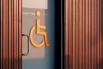 Accessible wheelchair restroom sign on glass sliding door with wooden wall in public area