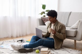 Teenager using laptop and drinking coffee during his online studies at home