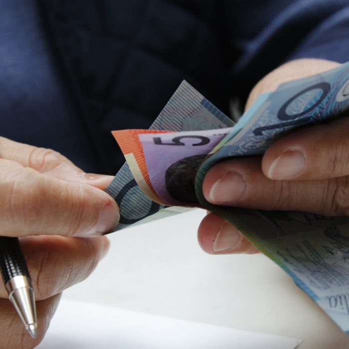hands of a senior woman holding australian banknotes and a pen