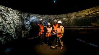 Miners standing in the centre of the AVIE 3D visualisation system, looking at a VR projection of an underground mine.