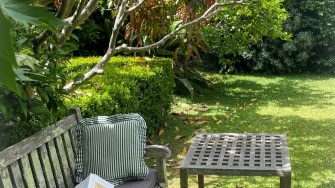 An outdoor bench furnished with a cushion, book, and glasses