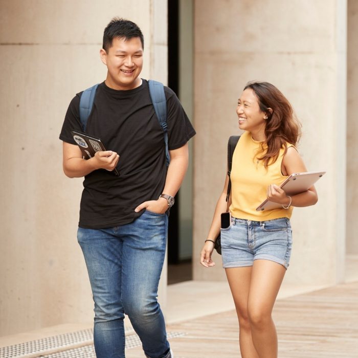 2 students walking with laptops and backpacks