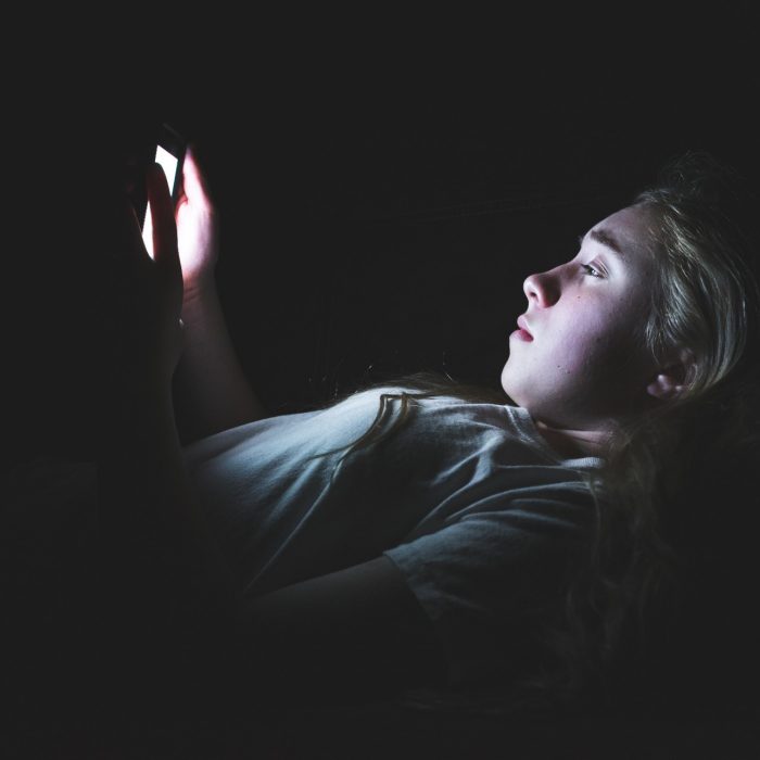 Depressed girl lying down on a couch in the dark while using her smartphone. The light from the screen is illuminating her face.