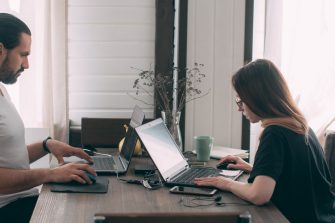 A man and a woman are working at a table at home. Married couple sit at a table in the living room with laptops. A guy and a girl work from home during quarantine