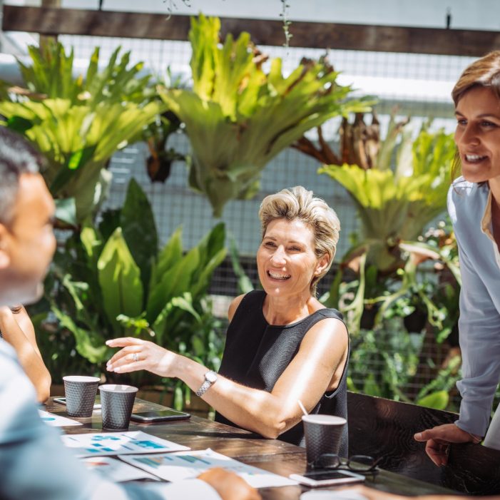 Group of professionals having a business meeting in outdoor cafe or restaurant where they discuss the investment ideas and cooperation plans while drinking coffee. Group of businesswomen and businessmen enjoying working together