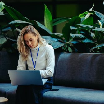 A woman sitting on a sofa, working on her laptop.