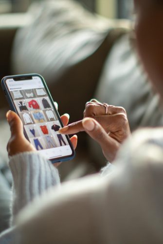 Person relaxing on a couch while browsing online shopping websites on a mobile device.