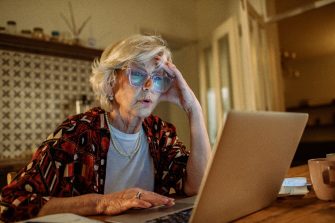 Worried elderly woman looking at laptop while managing finances at night