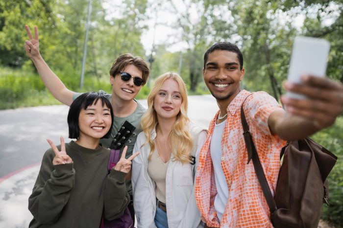 happy african american man taking selfie with interracial friends showing victory signs,stock image