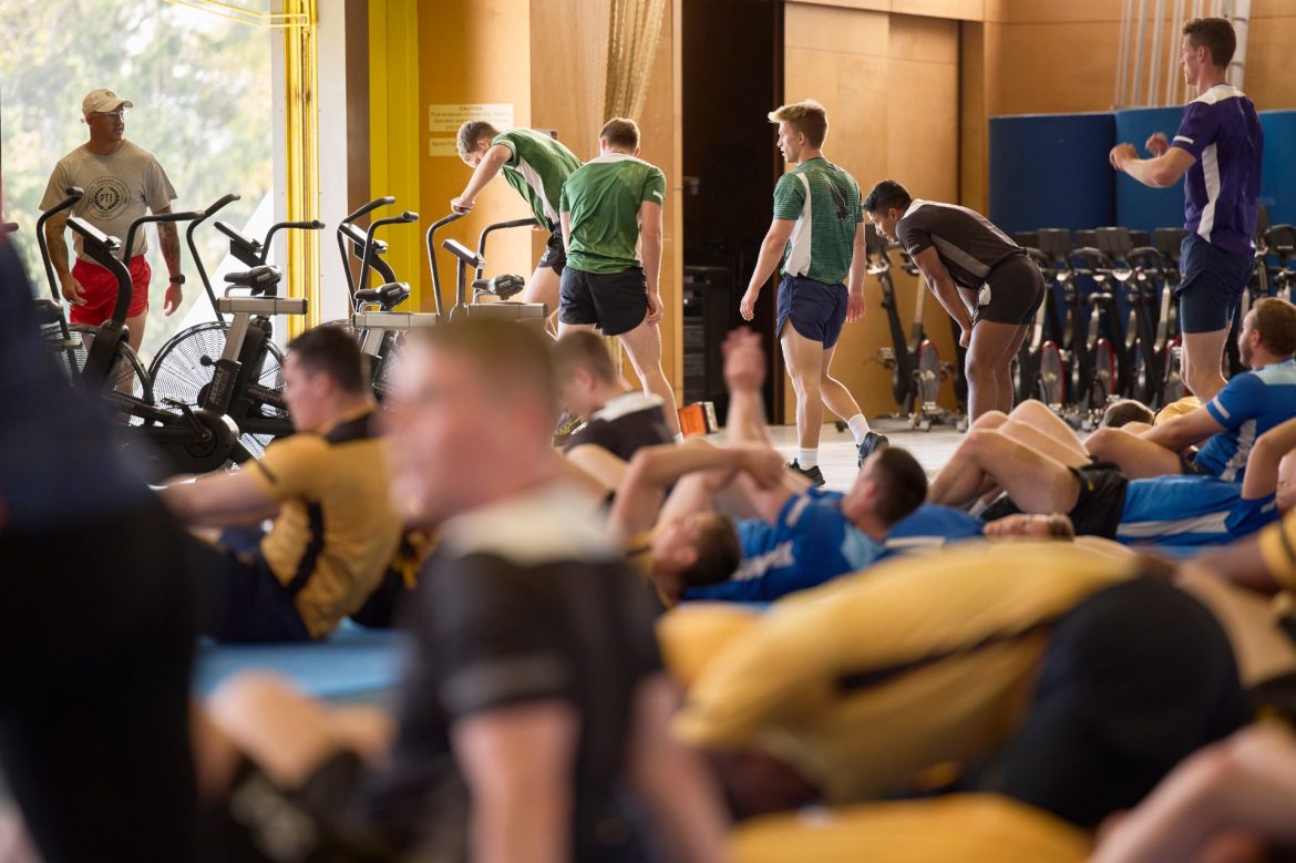 Indoor gym with people exercising and a coach looking on