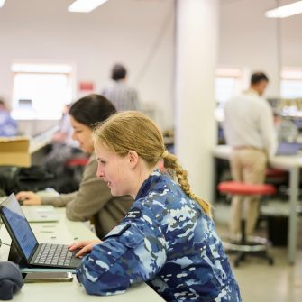 Student in military uniform studying on a laptop in a classroom