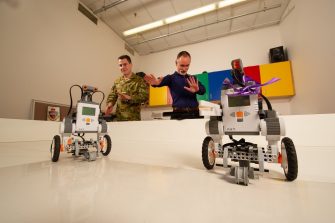 Officer Cadet Todd Baldwin (left) and Spike (Dr. Michael Barlow - right) playfully brainstorm alternate, gesture-based control schemes for the robots picture in the foreground; within the Machine Learning & Developmental Robotics (MLDR) lab.School of Engineering and Information Technology (SIET) Machine Learning & Developmental Robotics (MLDR).