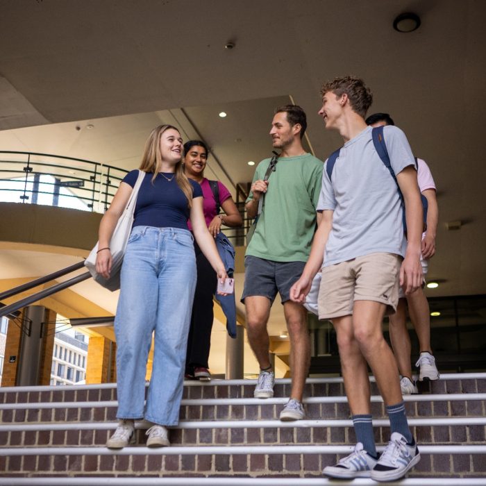A group of students chatting while walking down a staircase in front of the Quad Food Court