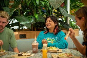 Students chatting while eating food at a table indoors on Kensington Campus
