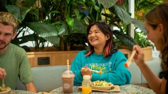 Students chatting while eating food at a table indoors on Kensington Campus