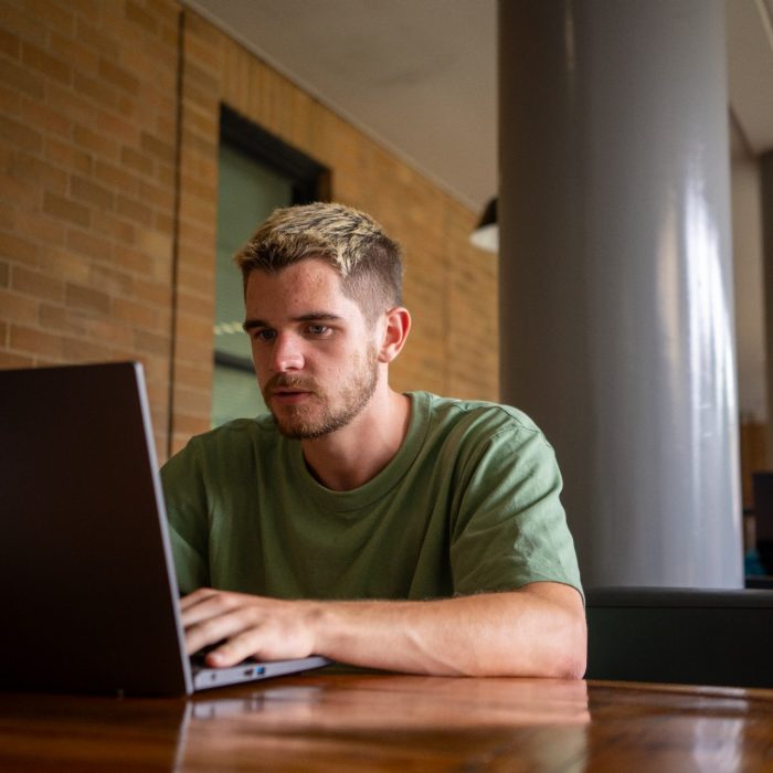 Students sitting at an outdoor table in the Quadrangle Building with their laptops