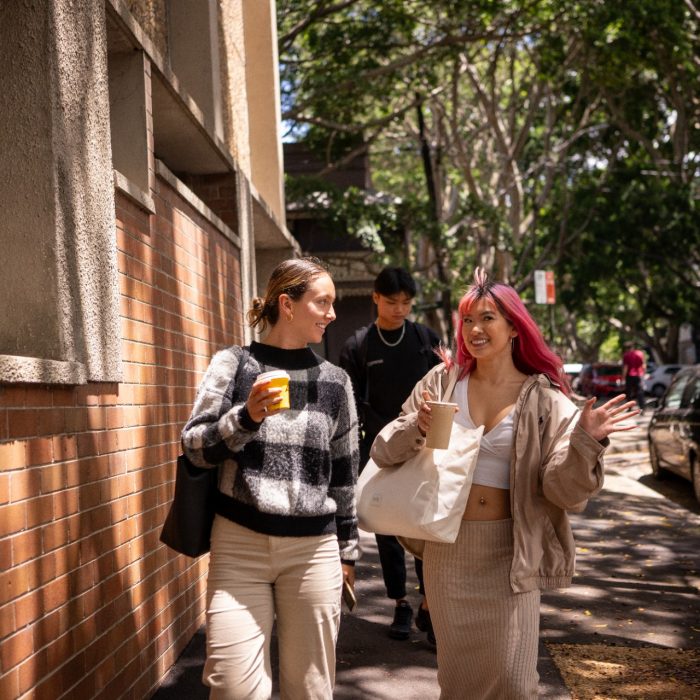 Two students chatting while holding take-away cups and walking outside near Paddington Campus