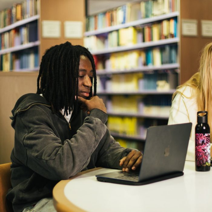 Students using their phones and laptops at a table in the library