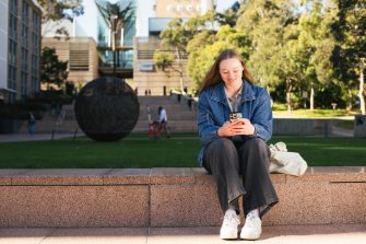 Student sitting by main walking using their phone
