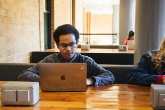 Students using their phones and laptops at the outdoor desks in the Quadrangle Building