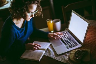 Young female student studying from a book and using laptop