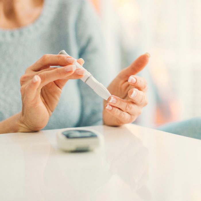 Mature woman doing blood sugar test at home in a living room. Selective focus to her finger.