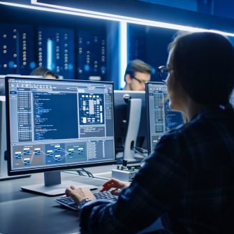 Smart Female IT Programer Working on Desktop Computer in Data Center System Control Room. Team of Young Professionals Doing Code Programming