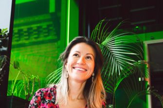 A woman sits with a laptop on her knee, smiling off camera