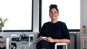 A woman sits in an office holding a mug and smiling off camera