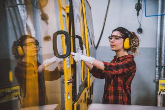 Portrait of apprentice engineering worker young woman working, examining and operating CNC plastic injection molding machinery in factory warehouse after studied manufacturing apprenticeship program certifies XXXL