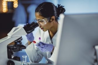 Biomedical engineer looking through microscope in lab