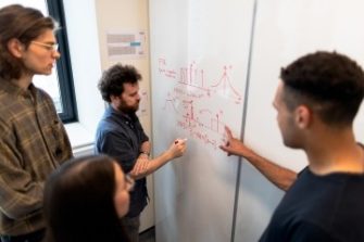 four Engineering students writing on and viewing whiteboard