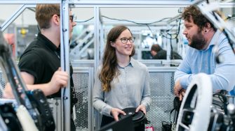 Three engineers standing together in a workshop discussing a project