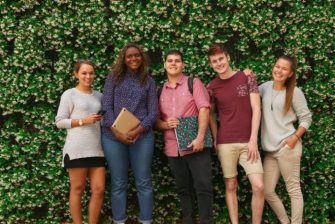 five students stand against a green backdrop smiling