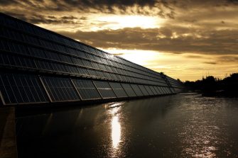 Solar panels over water, backlit by sunset