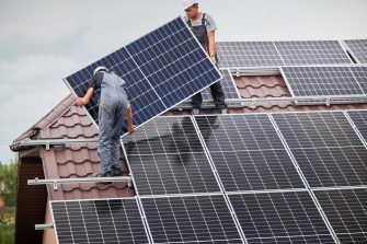 Technicians in blue suits mounting photovoltaic solar panels on roof of modern house. Solar modules as ecological renewable energy sources. Alternative production modules power sustainable resources