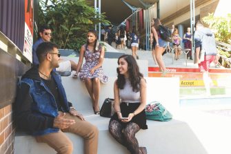 Students sit on the rainbow steps on a sunny day in the Kensington Quad