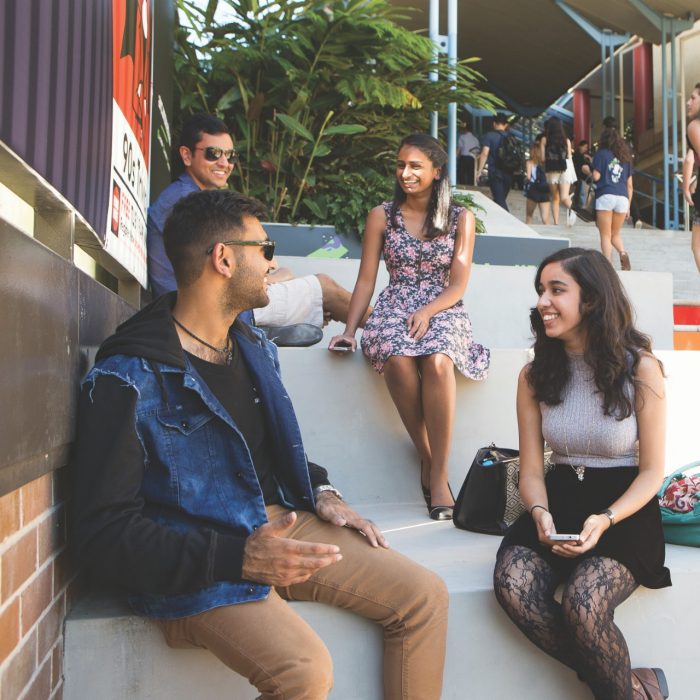 Students sit on the rainbow steps on a sunny day in the Kensington Quad