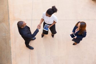 Business partners meeting in office hall. Top view of black man and woman in formal clothes shaking hands, holding tablet and talking. Partnership concept